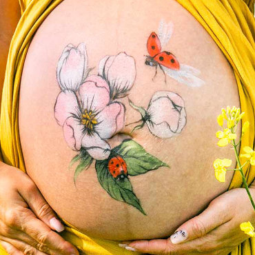 Bemalung auf Schwangerschaftsbauch mit einer Kirschblüte und Marienkäfer