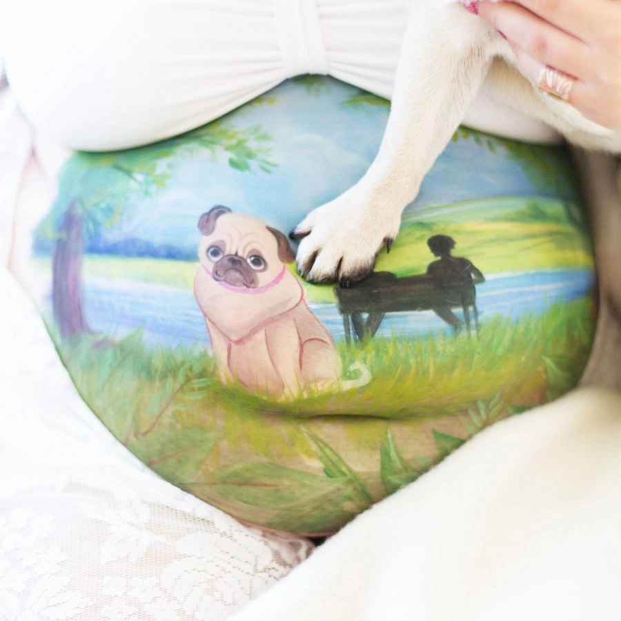 Babybauchbemalung mit Mops-Motiv, Hund legt seine Pfote liebevoll auf den bemalten Bauch