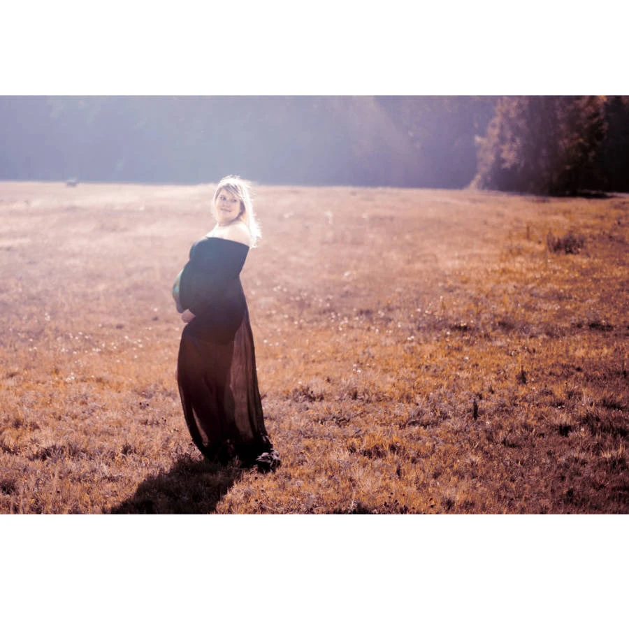 Babybauch-Shooting im langen Kleid auf einer Wiese – natürliche Outdoor-Aufnahme bei Sonnenlicht