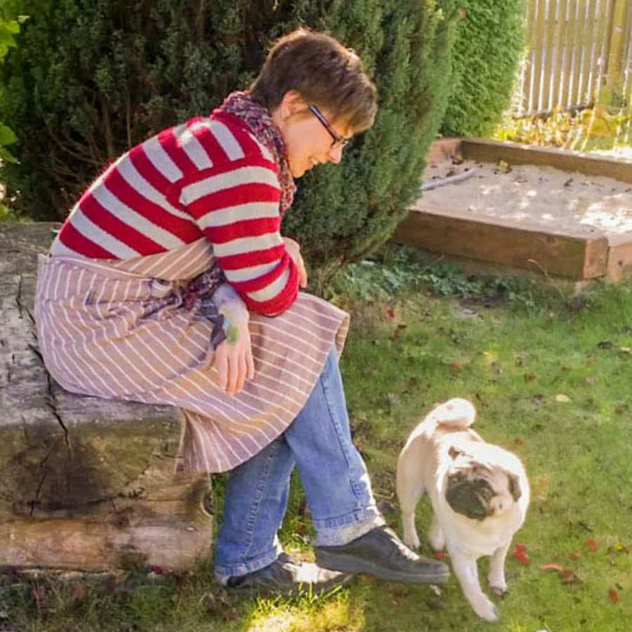 Künstlerin macht Pause im Garten und sitzt mit Mops während der Babybauchbemalung