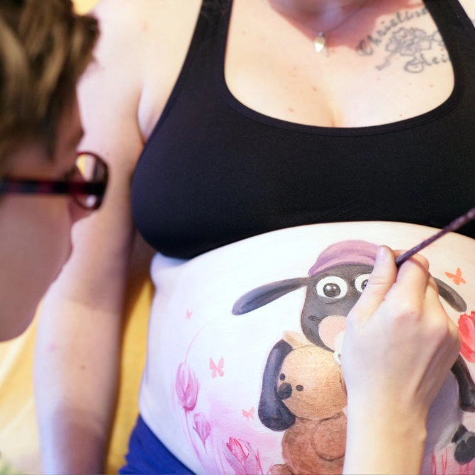 Babybauchbemalung mit Shaun das Schaf und Teddy – Künstlerin malt das Motiv auf den schwangeren Bauch