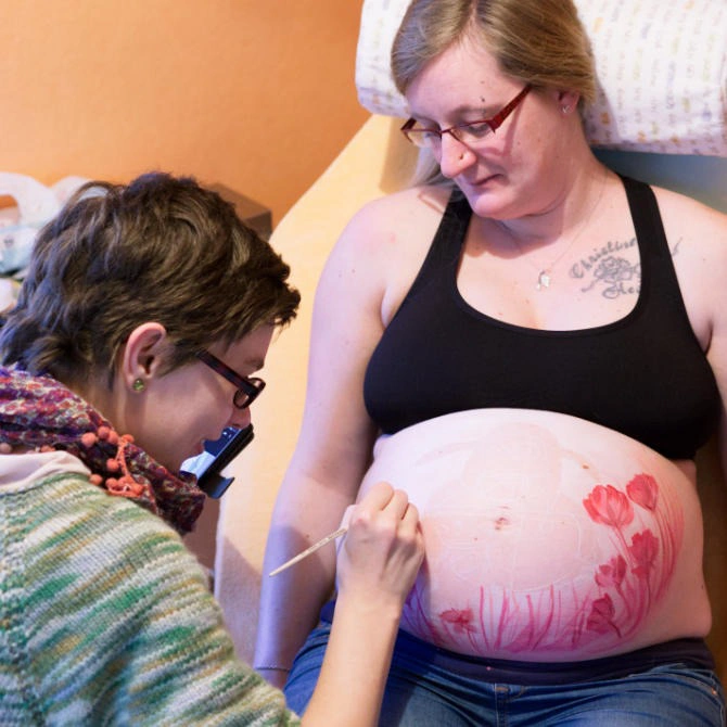 Künstlerin bemalt den Babybauch einer Schwangeren mit einem Tulpenmotiv – Entstehung der Babybauchbemalung