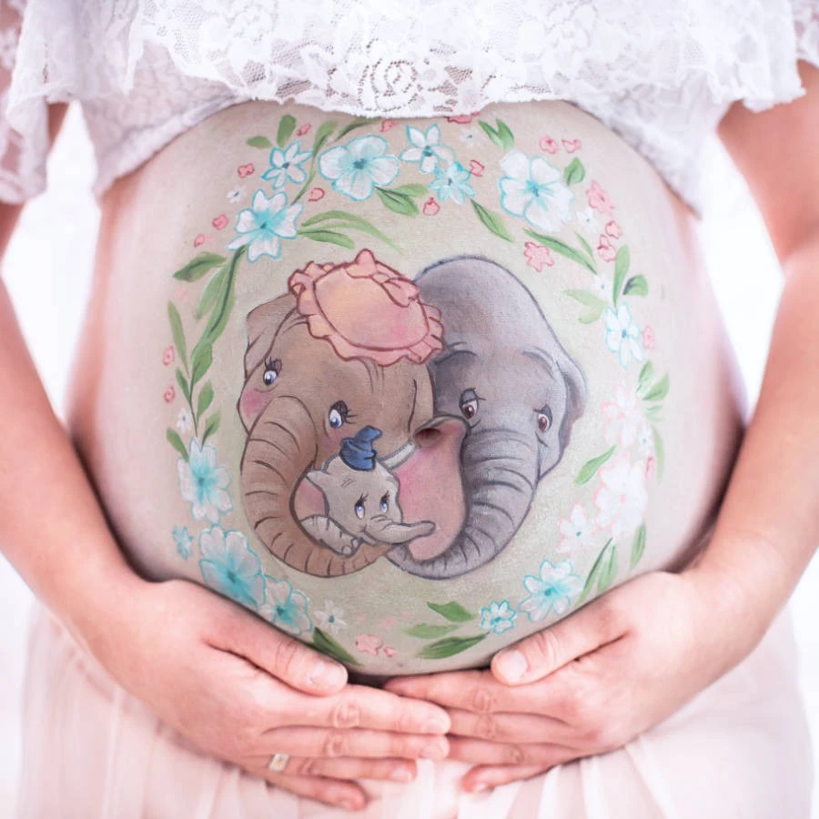 Detailaufnahme der Babybauchbemalung mit Dumbo-Motiv – Elefantenfamilie umrahmt von Blumen auf dem schwangeren Bauch