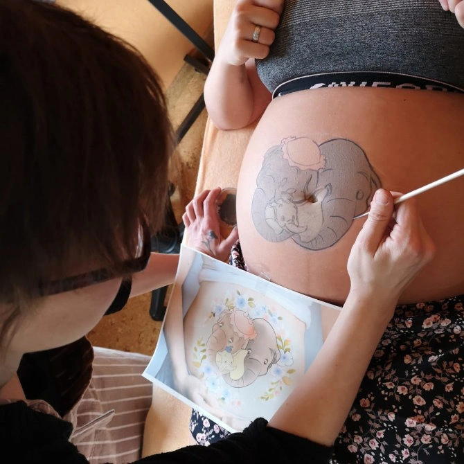 Entstehung einer Babybauchbemalung mit Dumbo-Motiv – Künstlerin malt den schwangeren Bauch nach Vorlage