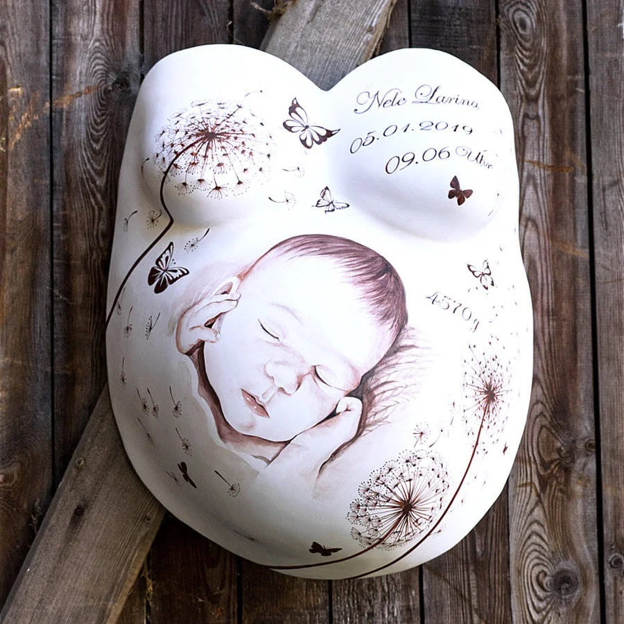 Liebevoll gestalteter Gipsabdruck eines Babybauchs mit Babygesicht, Pusteblumen und Schmetterlingen – personalisierte Erinnerung an die Geburt von Nele