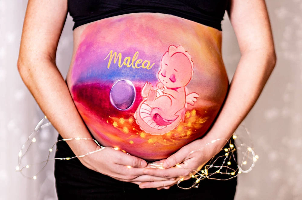 Bemalung auf Schwangerschaftsbauch mit einem Babydrachen in rosa
