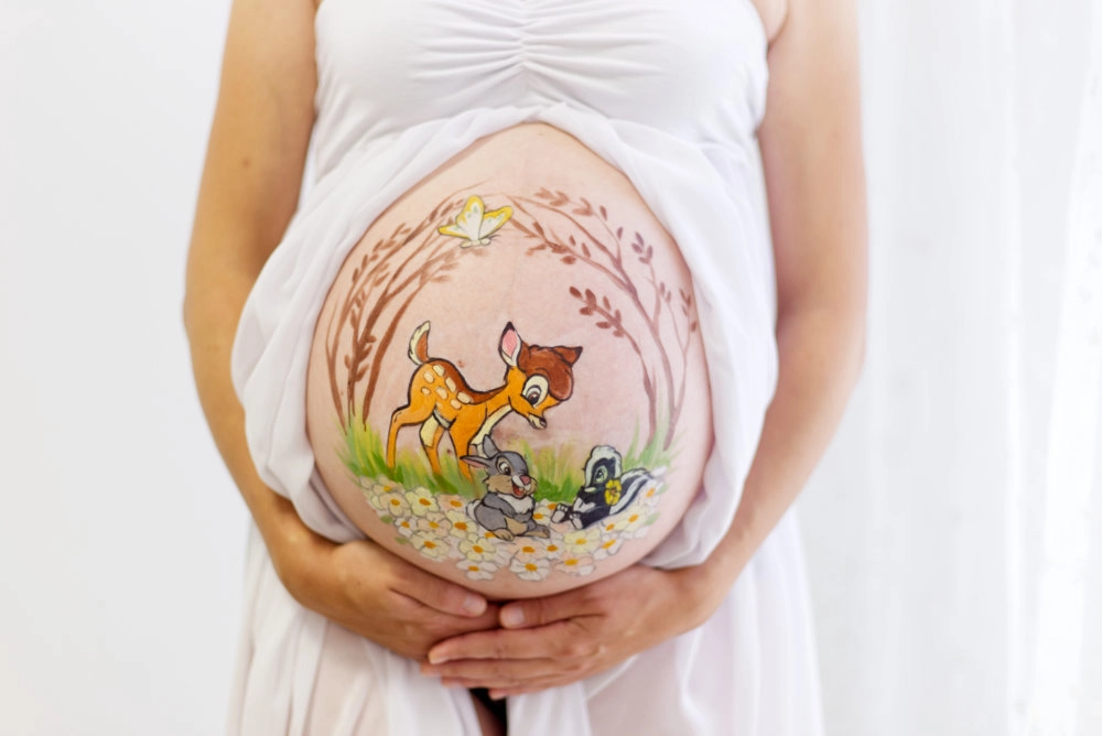 Verspielte Babybauchbemalung mit Bambi und seinen Freunden auf einer Blumenwiese – liebevolles Motiv für Natur- und Tierliebhaber
