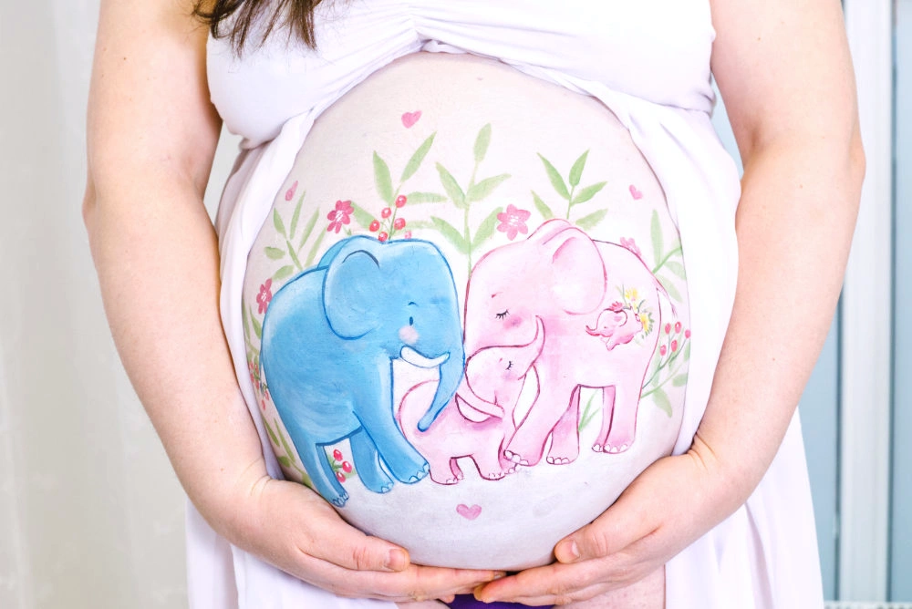 Liebevolle Babybauchbemalung mit einer rosa-blauen Elefantenfamilie – fröhliches Familienmotiv mit Herz und Blumen, perfekt für werdende Eltern