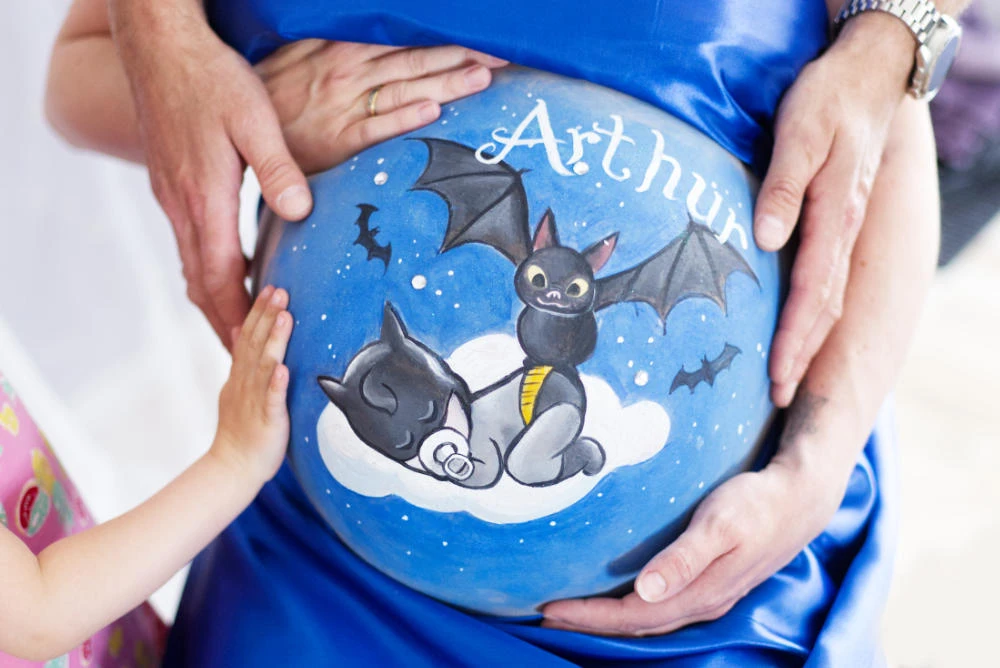 Kreative Babybauchbemalung mit schlafendem Fledermausbaby auf einer Wolke, umgeben von Sternen und kleinen Fledermäusen – personalisiertes Nachtmotiv mit dem Namen Arthur für ein unvergessliches Familienfoto