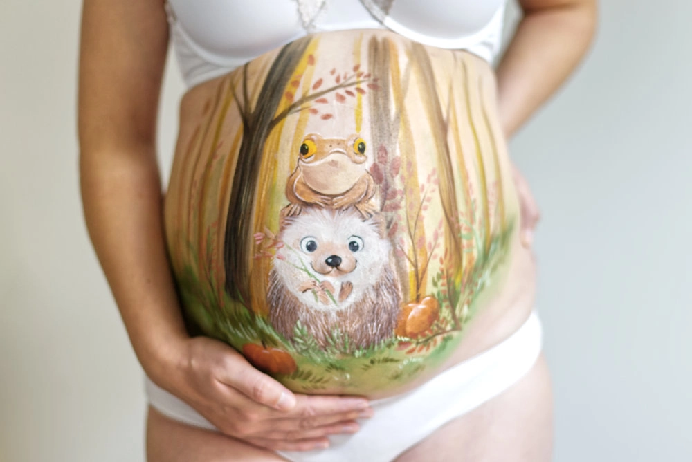 Niedliche Babybauchbemalung mit Igel und Frosch im herbstlichen Wald – liebevolles Naturmotiv für herbstliche Schwangerschaftsshootings