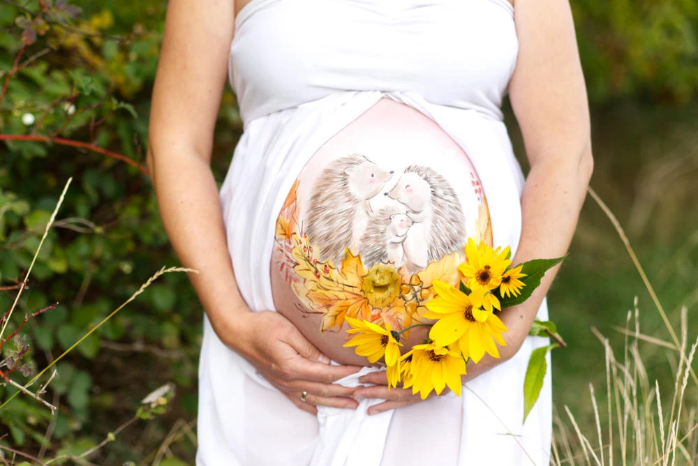 Herbstliche Babybauchbemalung mit einer liebevoll gestalteten Igelfamilie, umgeben von bunten Blättern und Sonnenblumen – natürliches Motiv als besondere Erinnerung an die Schwangerschaft