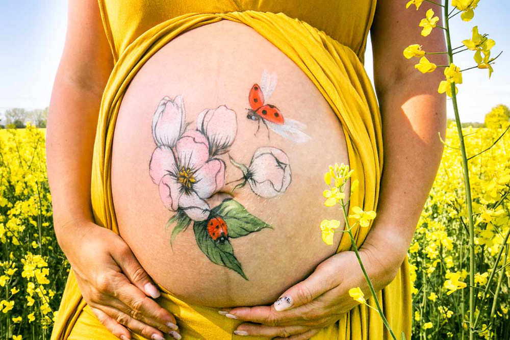 Bemalung auf Schwangerschaftsbauch mit einer Kirschblüte und Marienkäfer