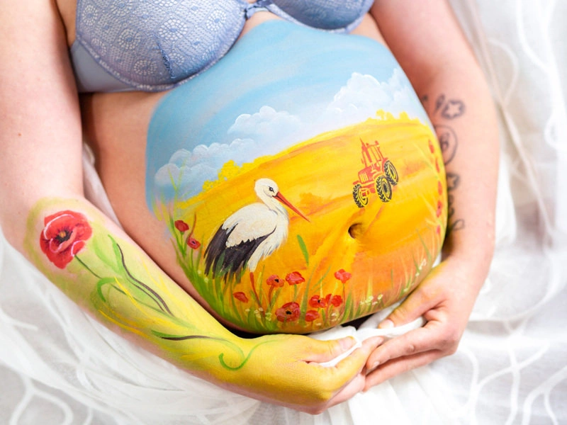 Bemalung auf Schwangerschaftsbauch mit Storch auf Feld mit Mohnblumen
