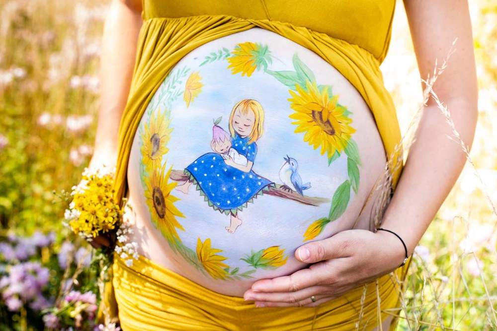 Bemalung auf Schwangerschaftsbauch mit einem Mädchen mit Sonnenblumen

