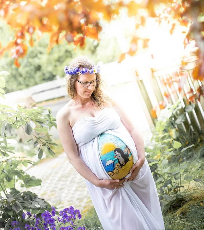 Babybauchbemalung mit Maulwurf-Motiv und Sonnenlandschaft – Outdoor-Shooting mit Blumenkranz und weißem Kleid