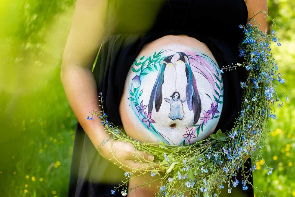 Bemalung auf Schwangerschaftsbauch mit einer Pinguinfamilie
