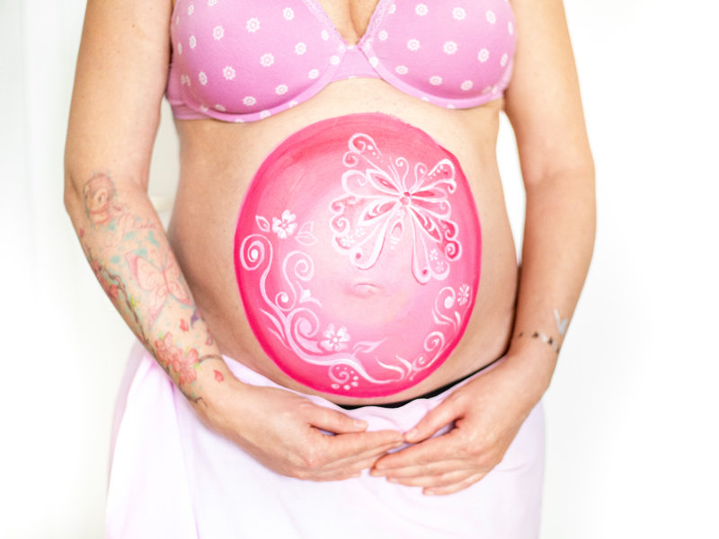 Bemalung auf Schwangerschaftsbauch mit Schmetterling auf rosa Hintergrund