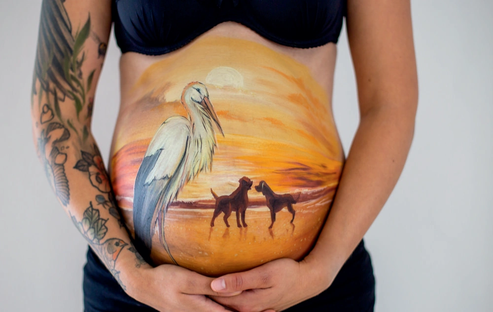 Bemalung auf Schwangerschaftsbauch mit Storch und Hunden
